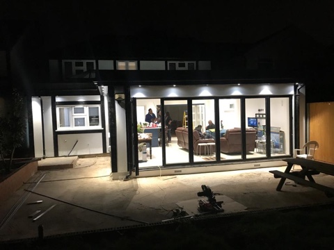 Bi-folding doors on a lit rear extension at night